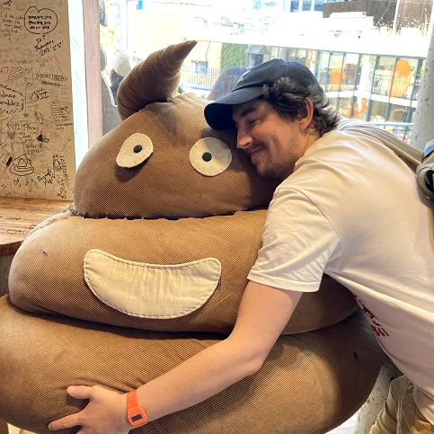 Sim smiling with his eyes closed whilst hugging a massive poop emoji plushie. He clealy loves South Korea.